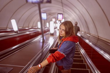Genç bir kadın metro istasyonuna inen yürüyen merdivenlerde duruyor..