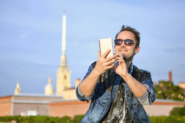 Genç gülümseyen adam, Rusya 'nın tarihi merkezi Saint-Petersburg' un arka planında akıllı telefon ekranına bir mesaj yazıyor..