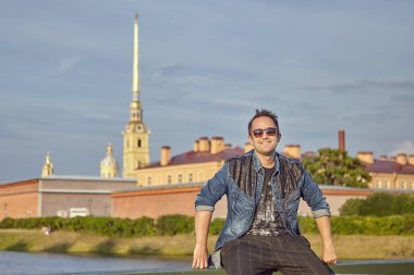 Gülümseyen turist, Rusya 'nın Saint-Petersburg kentinin tarihi mimarisinin arka planında oturuyor. Şehir merkezinde güneş gözlüklü genç beyaz adam..