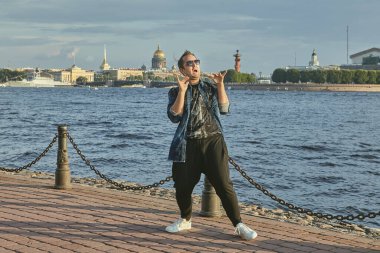Genç adam dans ediyor ve Rusya 'nın tarihi merkezi Saint-Petersburg' un arka planında yüzünü buruşturuyor. Güneş gözlüklü turist şehirde dans ediyor.