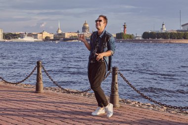 20 yaşındaki adam Saint-Petersburg gezisi sırasında Neva nehrinin rıhtımında dans ediyor. Genç erkek Rusya üzerinde seyahat ediyor..