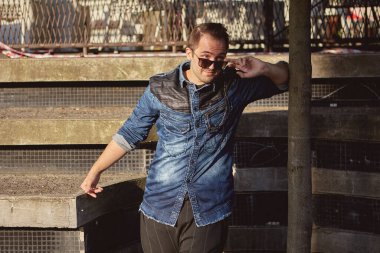 Genç bir adam gölgelerden birini izliyor. Beyaz erkek gözlüklerin altından dışarı bakar..