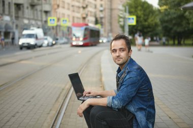 Kafkasyalı bir adam, bir tramvayı beklerken elinde defteriyle demiryolu hattına tehlikeli bir şekilde yakın oturuyor..