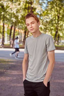Young caucasian handsome man is standing in the public park on the blurred background. clipart