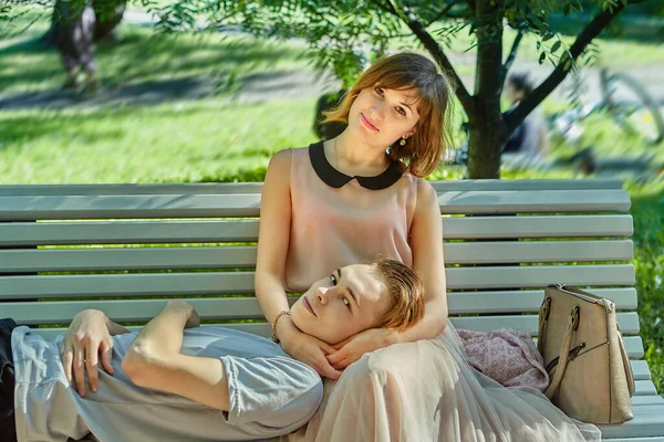 Genç ve güzel bir kadın, erkek arkadaşının kafası dizlerinin üzerinde bankta oturuyor. Kafkasyalı çiftin parka randevusu var..