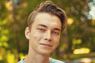 20 'li yaşlarda gülümseyen genç bir Rus' un yakın plan portresi güneşli bir havada halka açık bir parkın arka planında seçici bir odak ile çekilmiş. Bakışları olan 23 yaşında beyaz bir erkek..