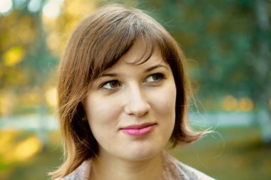 Yazın güneşli bir havada bir parkın arka planına bakan gülümseyen kahverengi gözlü bir kızın yakın çekimi..