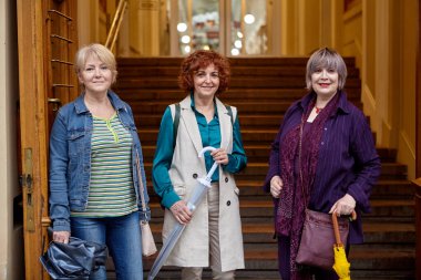 Üç yaşlı kadın alışveriş merkezinin girişinde duruyor..