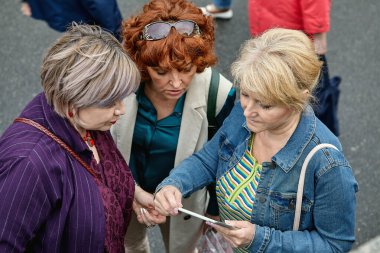 Sokakta konuşan üç üst düzey Avrupalı kadın. Bir grup Kafkasyalı kadın, yabancı bir şehri dolaşmak için bir tablet bilgisayar kılavuzu kullanıyor..