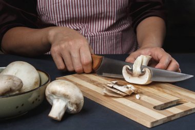 Önlüklü bir kadın bıçakla mantar kesiyor.