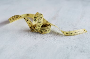 Sarı şerit, santimetre cinsinden, kıvrılmış. Tahta bir masanın üzerindeki şeridi yakından ölçmek.