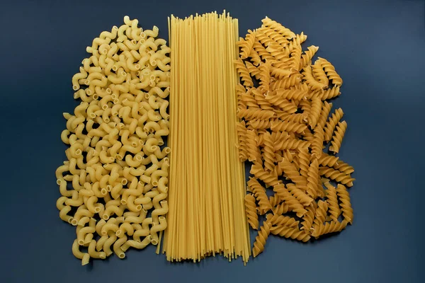 Mix of pasta on a dark background. Three varieties of pasta. Spaghetti pasta and two different varieties of spiral pasta