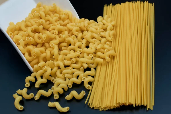 Small spring-shaped pasta is poured out of a white saucer. Spaghetti pasta on a dark background. close-up
