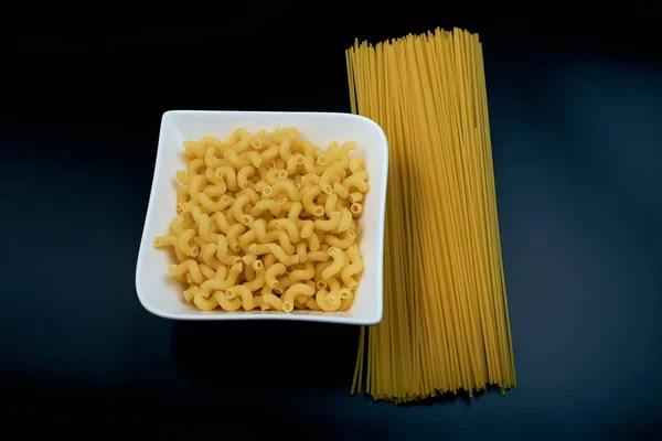 Small pasta in the shape of a spring in a white plate Spaghetti pasta on a dark background. top view.