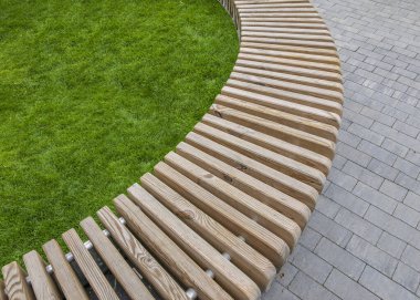 Düz ahşap bloklardan oluşan eğri bir sıra şeklinde bir park bankı.