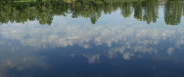 Bulutlu mavi gökyüzü suya yansıyor.