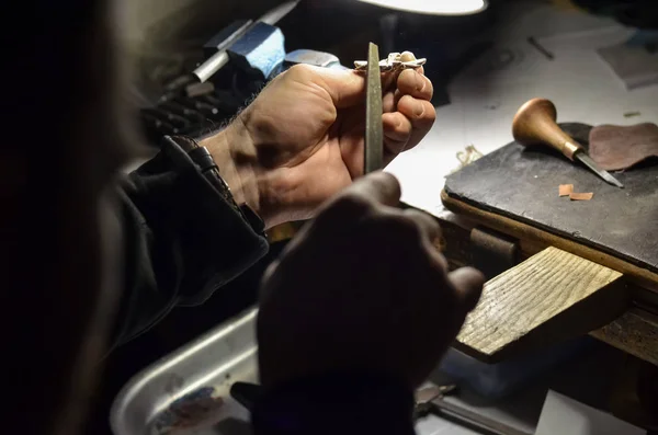 The master jeweler holds the working tool in his hands and makes jewelery at his workplace in the jewelry workshop.