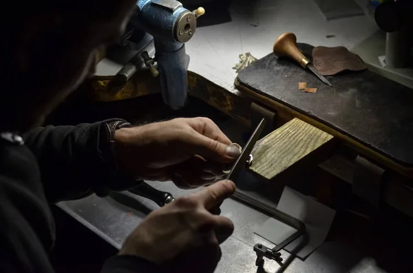 The master jeweler holds the working tool in his hands and makes jewelery at his workplace in the jewelry workshop.