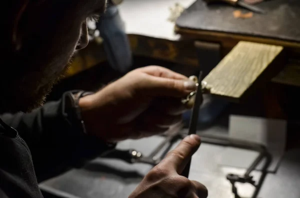 The master jeweler holds the working tool in his hands and makes jewelery at his workplace in the jewelry workshop.