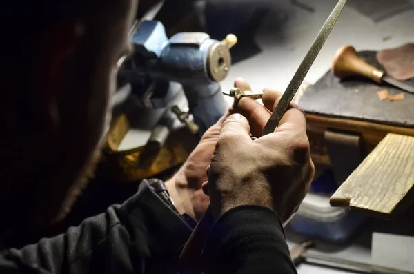 The master jeweler holds the working tool in his hands and makes jewelery at his workplace in the jewelry workshop.