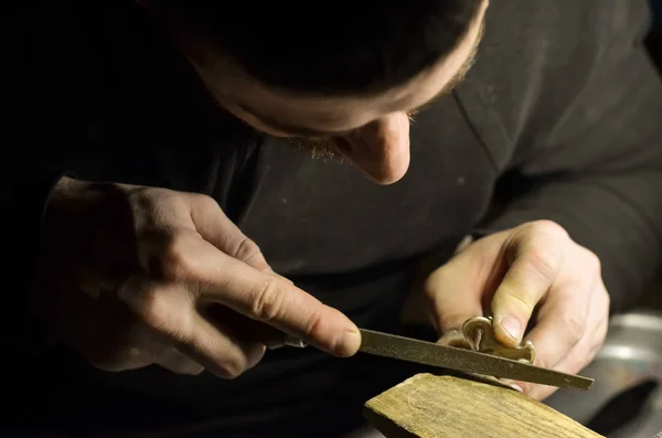 The master jeweler holds the working tool in his hands and makes jewelery at his workplace in the jewelry workshop.