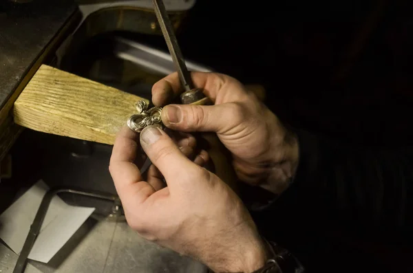 The master jeweler holds the working tool in his hands and makes jewelery at his workplace in the jewelry workshop.