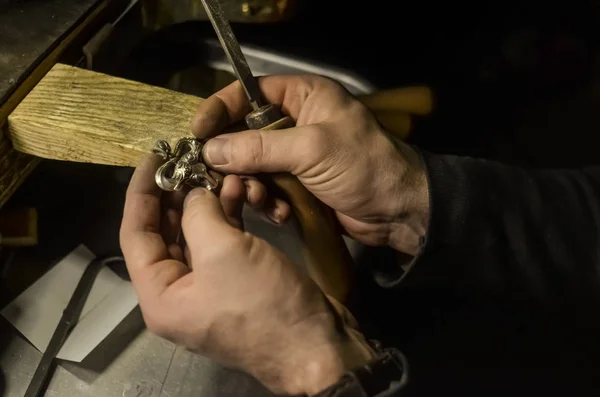 The master jeweler holds the working tool in his hands and makes jewelery at his workplace in the jewelry workshop.