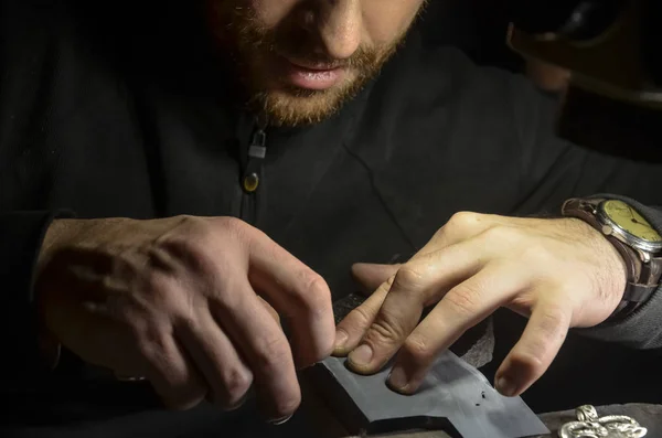 The master jeweler holds the working tool in his hands and makes jewelery at his workplace in the jewelry workshop.