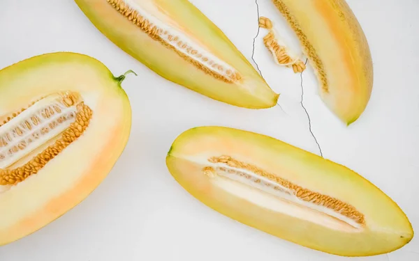 Yellow ripe sweet melon with seeds cut into pieces on white cracked in the background.