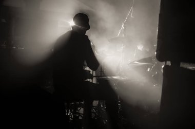 Sahne ışıklarının altında davul çalan bir davulcunun silueti. Rock konseri.