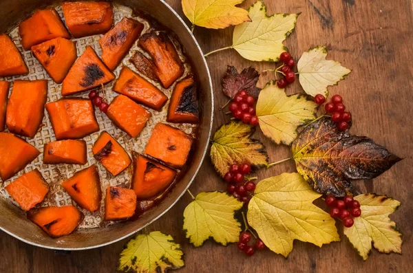 Fried baked on grill pumpkin, a traditional autumn snack.Warm dish as a dessert.On a baking sheet, on a rustic wooden old table with yellow leaves and viburnum.Top view copy space,food for Halloween