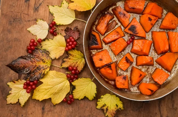 Fried baked on grill pumpkin, a traditional autumn snack.Warm dish as a dessert.On a baking sheet, on a rustic wooden old table with yellow leaves and viburnum.Top view copy space,food for Halloween