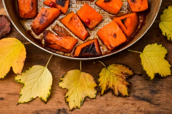 Fried baked on grill pumpkin, a traditional autumn snack.Warm dish as a dessert.On a baking sheet, on a rustic wooden old table with yellow leaves and viburnum.Top view copy space,food for Halloween