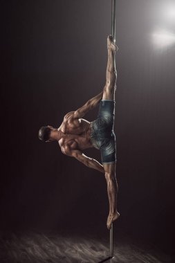 Pole 'de bir adam orta bölünme yapıyor. Siyah arka planda kutup dans kas atlet. Güçlü erkek fitness modeli esnek bir hüner yürütür. 