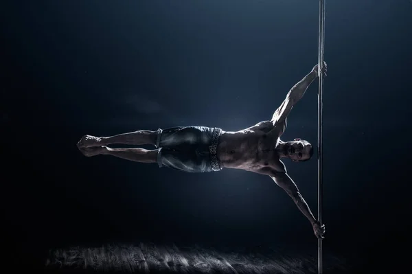 Pole dance male athlete. Strong and muscular guy executes a trick. Pole dancing world champion showing skills.