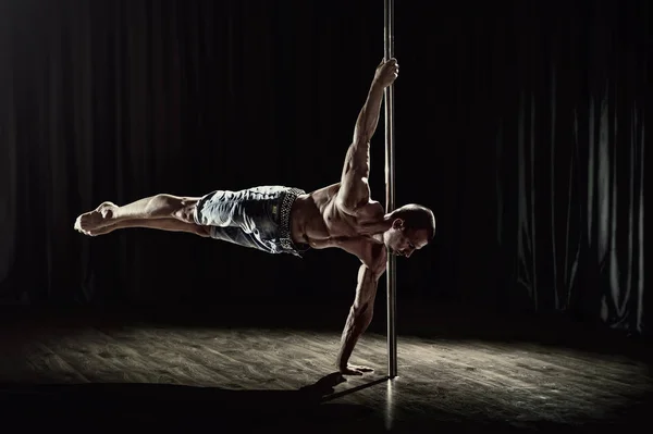 Pole dance male athlete. Strong and muscular guy executes a trick. Pole dancing world champion showing skills.