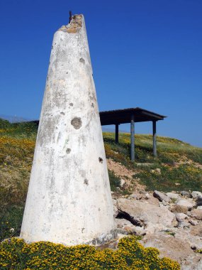 sarı bahar çiçekleri ve baf kıbrıs parlak mavi gökyüzü ile çevrili kıyı kayalıkları üzerinde bir barınak yanında kırık bir beyaz konik beton yapı