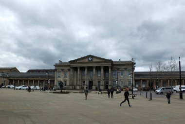 Huddersfield, West Yorkshire, İngiltere - 26 Nisan 2018: St Georges Meydanı'ndaki yayalar tarihi tren istasyonu binasının önünden geçiyor.