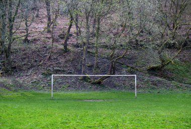 arka planda bir ormanlık tepe ile kırsal bir futbol sahası üzerinde boş futbol kale direkleri
