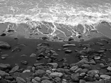 puerto de la cruz tenerife renkli çakıl ve taşlarla siyah bir kum plajda kırma beyaz sörf monokrom görüntü