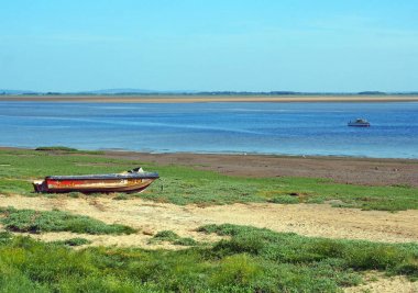 nehir üzerinde küçük bir balıkçı teknesi ve çim kaplı kum ve parlak mavi kaynama gökyüzü ile kıyıda eski terk edilmiş sürat teknesi ile lancashire ribble haliç görünümü