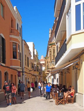 Turistler ve alışveriş yürüyüş ve Ciutadella Menorca şehir merkezinde sokakta bir açık hava kafede oturan
