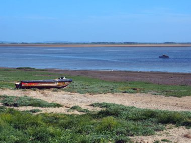 nehir üzerinde küçük bir balıkçı teknesi ve çim kaplı kum ve parlak mavi yaz gökyüzü ile kıyıda eski terk edilmiş sürat teknesi ile lancashire ribble haliç görünümü