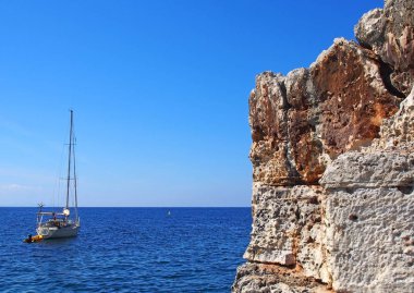 parlak mavi yaz güneşışığında küçük kıyı şeridinde güzel engebeli kayalıklar yanında parlak sakin Akdeniz'de bir yat