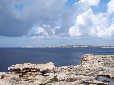 Sahil ve kayalık kayalıkların manzara görünümü sakin bir mavi deniz ve koy boyunca mesafe tatil binaları yansıyan ışık ile ciutalla menorca ayı