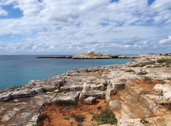 mavi yaz gökyüzü ile mesafede oyma kayalıklar ve eski bir fort ile menorca cala santandria de körfezin doğal bir görünüm