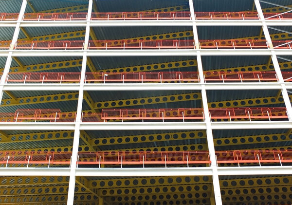 A looking upwards view of large modern commercial building under construction with steel beams and yellow girders with orange safety fences