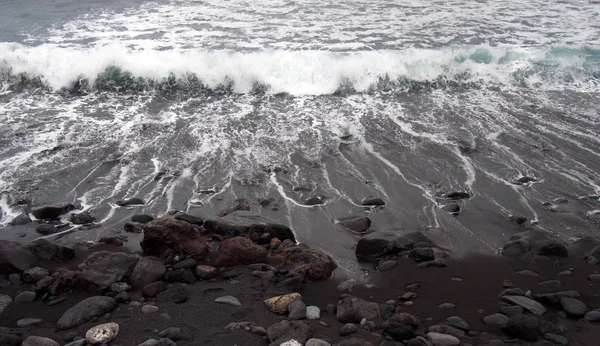 白浪冲破了一个黑色的沙滩上的彩色卵石和石子在Puthe Cruz Tenerife — 图库照片