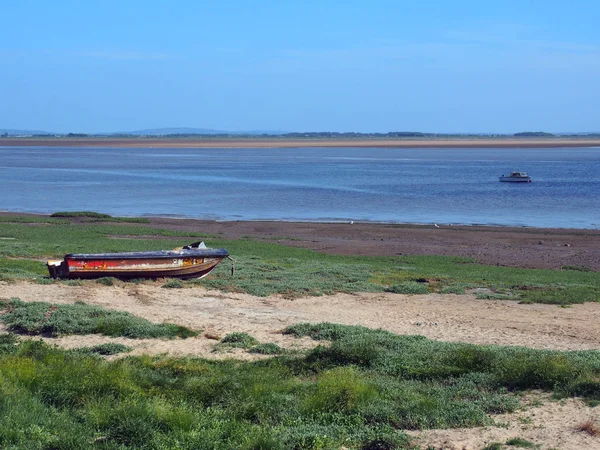 nehir üzerinde küçük bir balıkçı teknesi ve çim kaplı kum ve parlak mavi yaz gökyüzü ile kıyıda eski terk edilmiş sürat teknesi ile lancashire ribble haliç görünümü