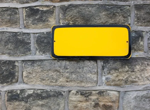 a blank yellow metal sign with empty space for copy text on an old stone wall background